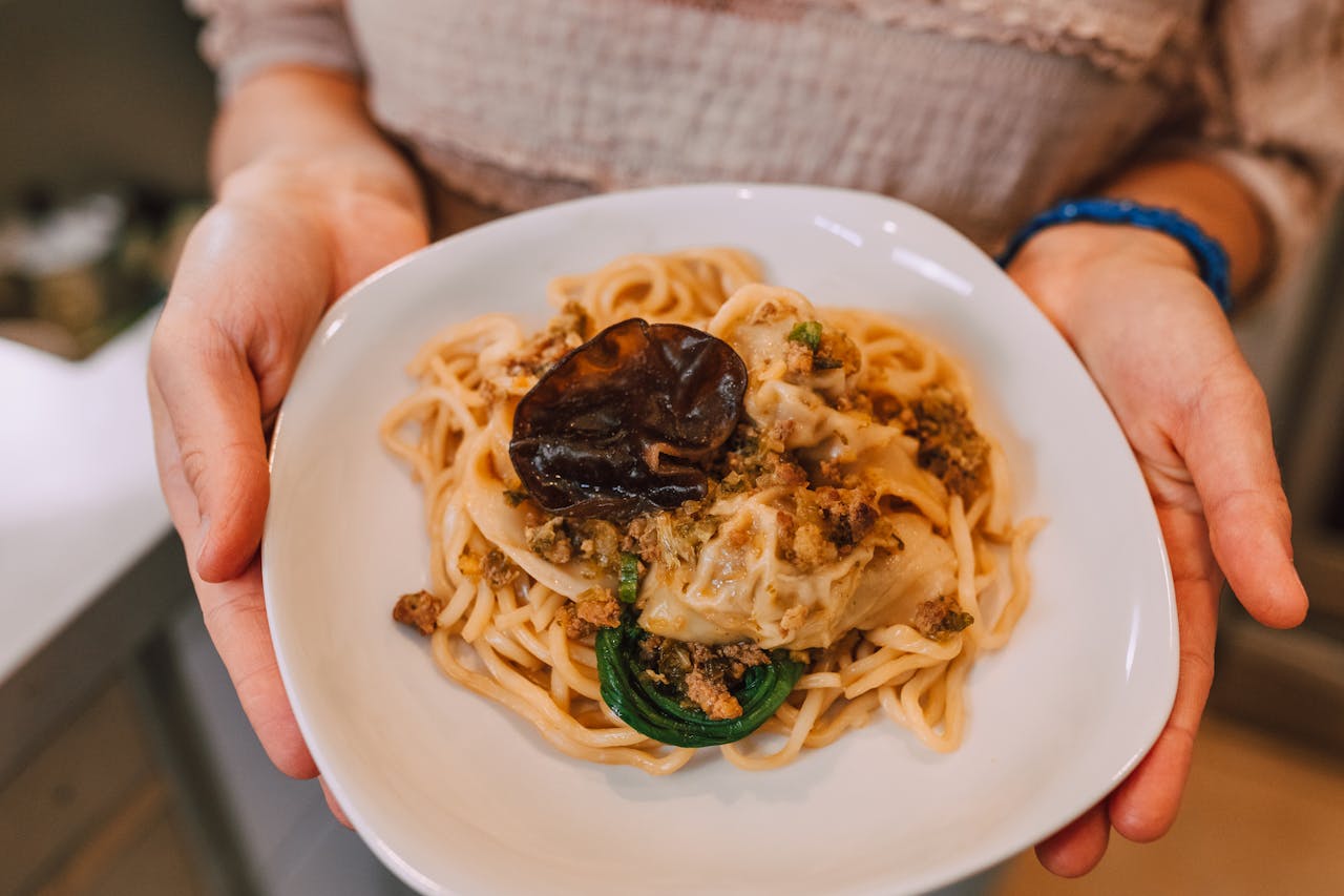 Close-up of creamy pasta with mushrooms, held in hands. Perfect for food photography enthusiasts.